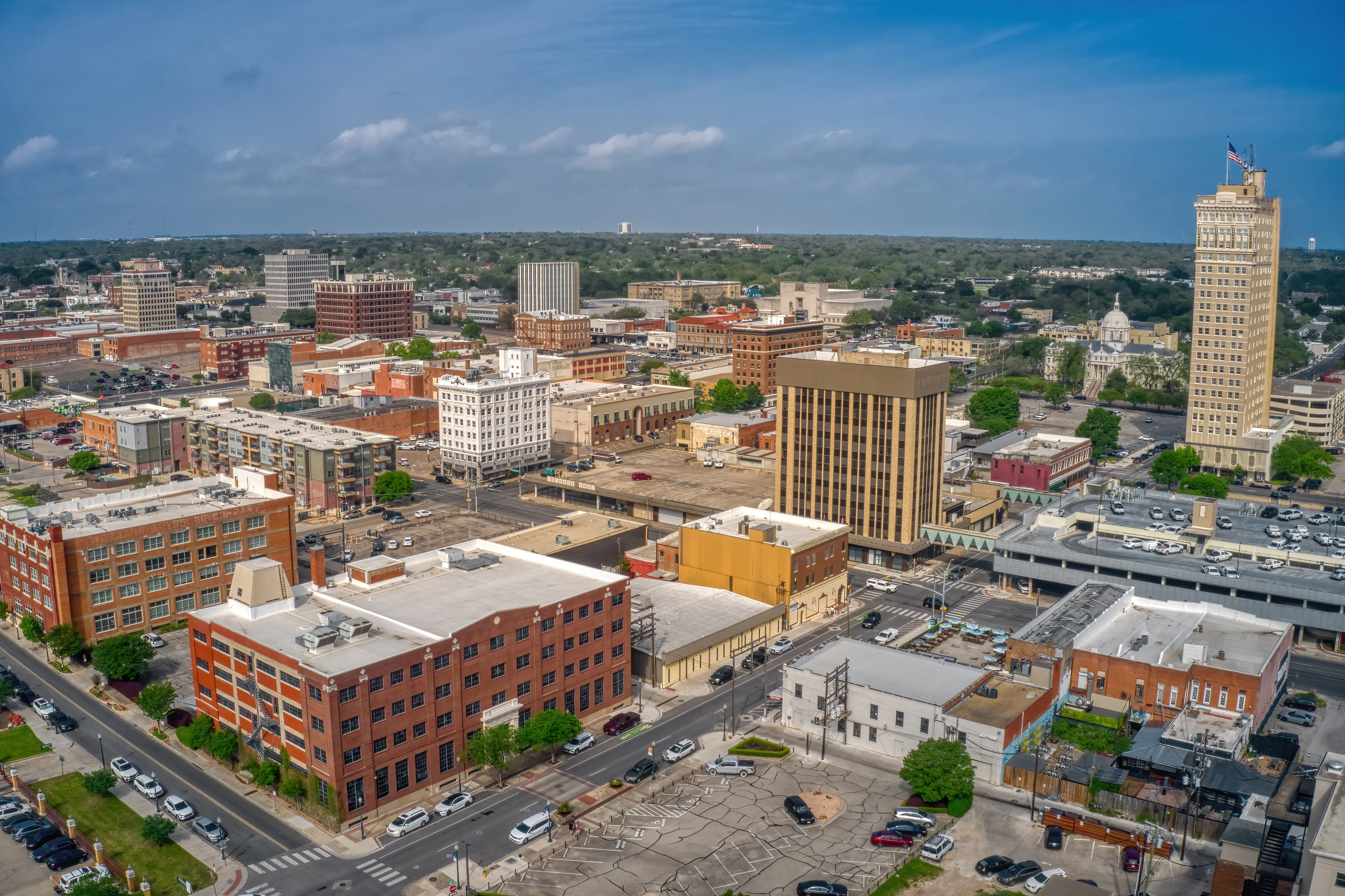 Aerial view of downtown Waco, Texas, with brick warehouse buildings in the foreground, a historic high-rise tower on the right and a domed courthouse behind it